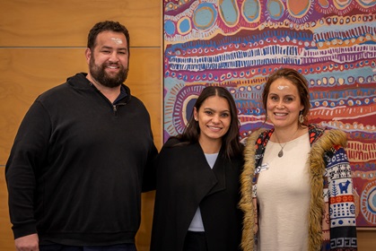 Three people standing in front of an Aboriginal painting